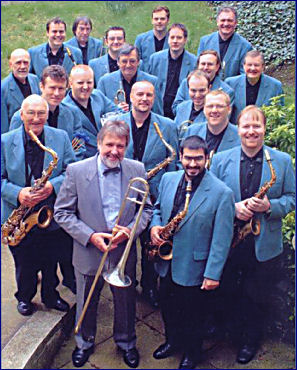 Jiggs Whigham and the BBC Big Band, viewed from above. Jiggs is wearing a suit and holding his trombone. The BBC Big Band are wearing pale blue jackets and dark shirts and holding their instruments.